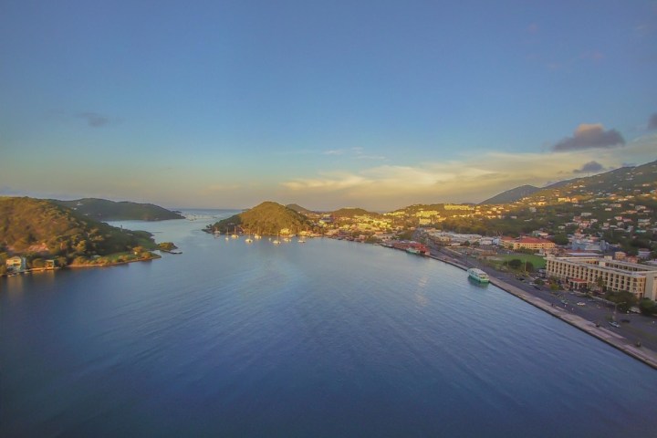 Aerial view of a coastal town with calm blue water and hillside buildings at sunset.